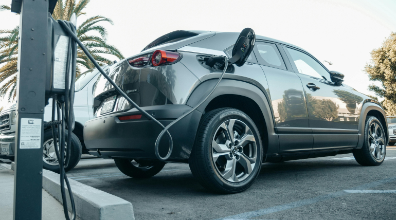 Gray electric SUV connected to a public EV charging station in a commercial parking lot.